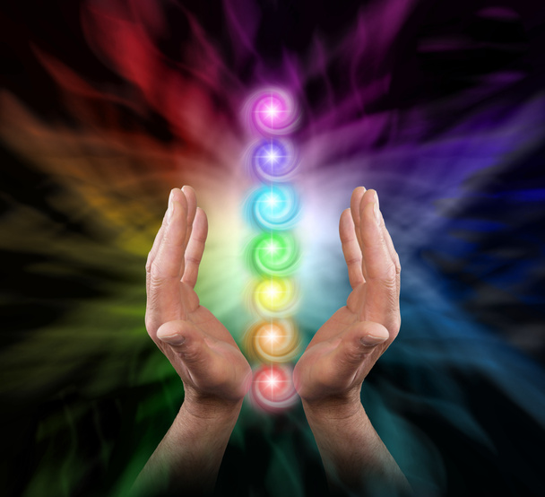 Sending Chakra Healing Energy - Male parallel hands facing upwards against a multicoloured background of energy and the Seven Chakras floating between his hands  - Photo, Image