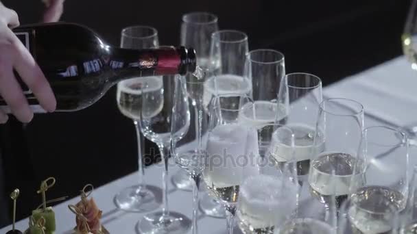 De ober giet de champagne in de glazen. Tabel van de bovenste vol glazen mousserende witte wijn met flessen op de achtergrond. - Video