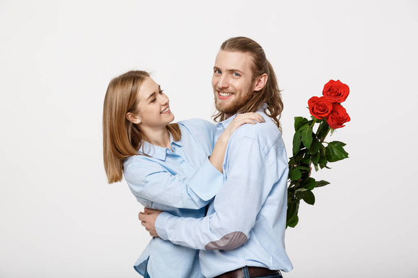 Portrét atraktivní mladý muž schovává květiny od jeho přítelkyně ještě předtím, než jí překvapení nad bílým pozadím izolované. - Fotografie, Obrázek