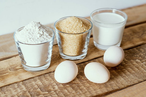 milk, flour, sugar and dough eggs on a wooden table - Foto, afbeelding