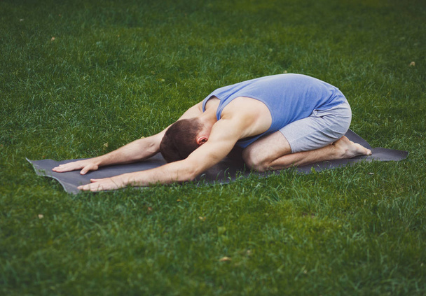 Young man training yoga in childs pose outdoors - Photo, Image