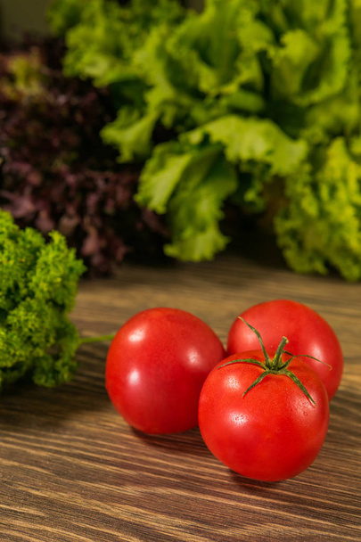 Juicy ripe tomatoes on a wooden table with fresh herbs in the background. Fresh vegetables. - Photo, image
