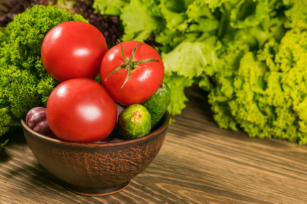 Red tomatoes and cucumbers, lettuce on a wooden table. Delicious vegetarian food. - 写真・画像