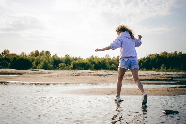 lovely young woman with curly hair, the romance of youth, a journey walk on a warm summer sunny day on a sandy beach with water - Foto, afbeelding