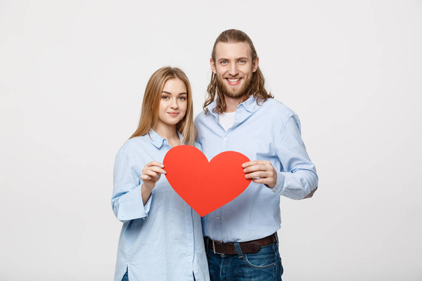 Portrait of young happy couple in love holding red paper heart. - Photo, Image