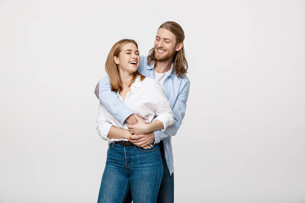 Portret van vrolijke jonge paar permanent en knuffelen elkaar op geïsoleerde witte achtergrond - Foto, afbeelding
