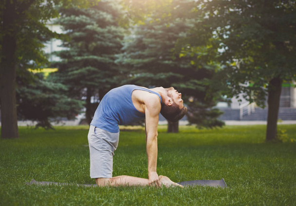 Man training yoga in camel pose outdoors - Foto, afbeelding