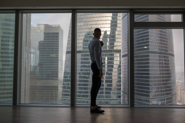 Uomo d'affari in piedi vicino a una grande finestra panoramica con grandi edifici della città
. - Foto, immagini