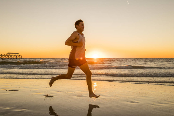  νεαρός δυναμικός αθλητής δρομέας άνθρωπος με fit ισχυρό σώμα κατάρτισης στο ηλιοβασίλεμα παραλία τρέχει ξυπόλητος σε υγιή και γυμναστήριο έννοια άθλημα το καλοκαίρι - Φωτογραφία, εικόνα