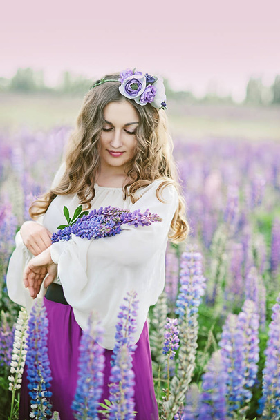 portrait of Beautiful young woman holding bouquet of lupine on field. The concept of nature and romance.  - Fotó, kép
