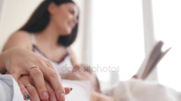 ソファの上幸せな若い魅力的なカップルの手で結婚指輪、女の子を読み取り本を彼女の膝の上の男の嘘 - 映像、動画