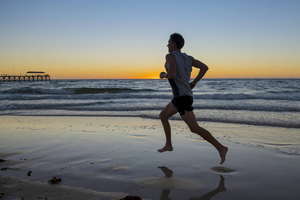 Silhouette junger dynamischer Athlet Läufer mit fit starkem Körpertraining am Sonnenuntergang Strandlauf barfuß im Sport gesundes Lifestylekonzept - Foto, Bild