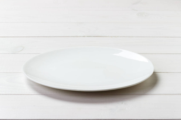 Biały okrągły talerz na tle biały drewniany stół. Widok perspektywiczny - Zdjęcie, obraz
