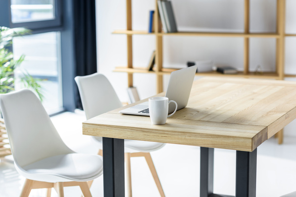 Portátil y taza de café en la mesa en la oficina moderna
 - Foto, imagen
