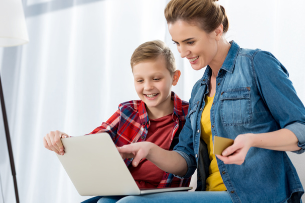 mooie moeder en zoon maken e-shopping met laptop en creditcard - Foto, afbeelding