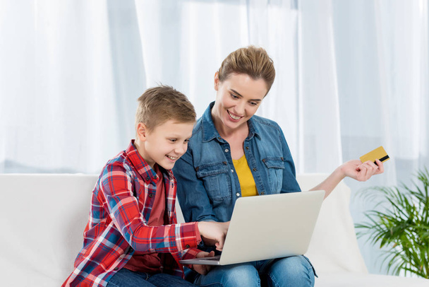 счастливые мать и сын совершают интернет-покупки с ноутбуком и кредитной картой
 - Фото, изображение