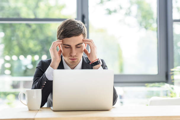 Businessman suffers from headache while working on laptop - Фото, изображение