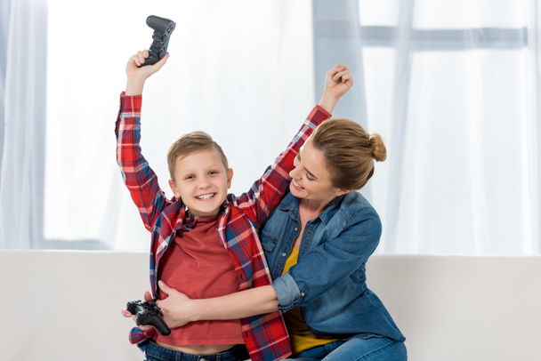 mother embracing her celebrating son while playing video games together - Photo, Image