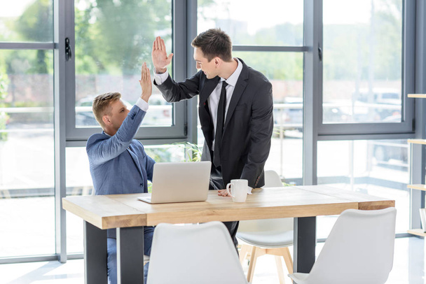 Successful businessmen giving high five by laptop in modern office   - Foto, Imagen