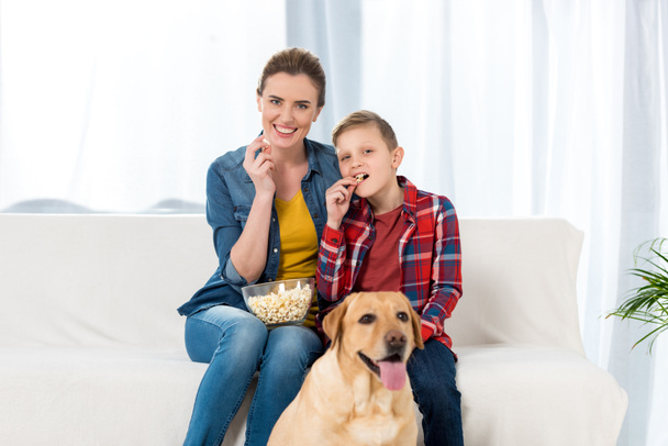 mother and son watching movie with popcorn while their dog sitting on floor - Photo, image