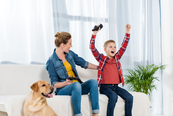 expressive mother and son playing video games while their dog sitting on floor - Photo, Image