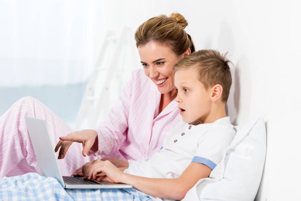 happy mother and emotional son using laptop together in bed - Foto, Bild