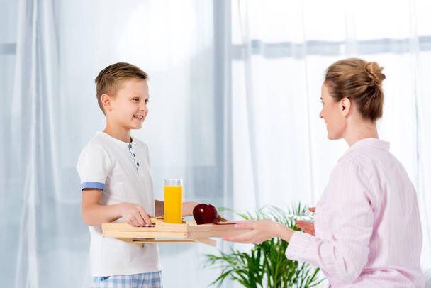 happy little son carrying breakfast on wooden tray for mother - Photo, Image