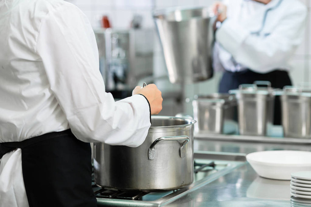 Chefs at stove in professional catering kitchen stirring in pots - Zdjęcie, obraz