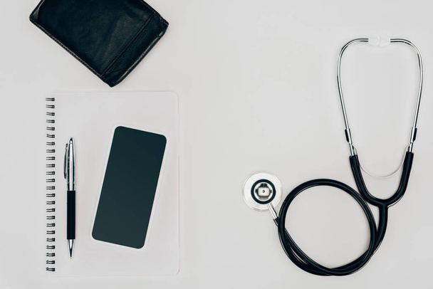 top view of medical stethoscope, notebook and smartphone on white surface - Foto, Imagen