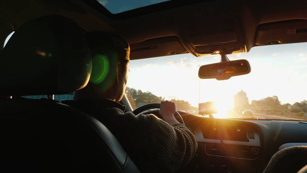 An Asian man drives a car along the highway, the setting sun shines in the windshield. Back view - Foto, Bild