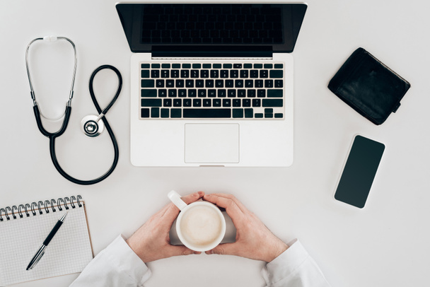 částečný pohled lékaře na pracovišti s notebookem, stetoskop a šálek kávy - Fotografie, Obrázek