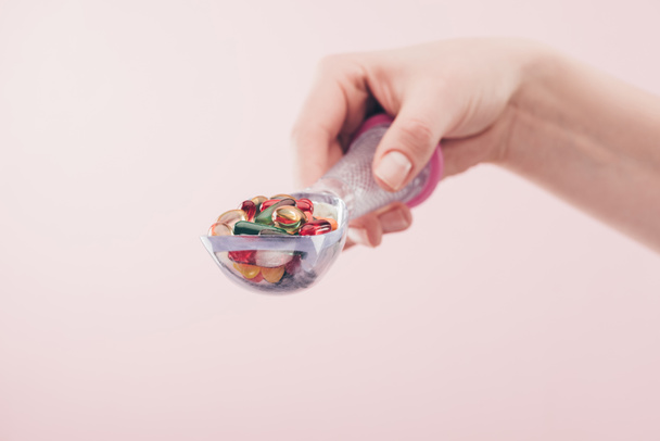 частичный вид женщины, держащей таблетки в ложке изолированы на розовый
 - Фото, изображение