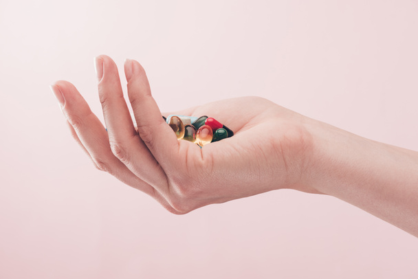 手で隔離されたピンクの丸薬を保持している女性の部分的なビュー - 写真・画像