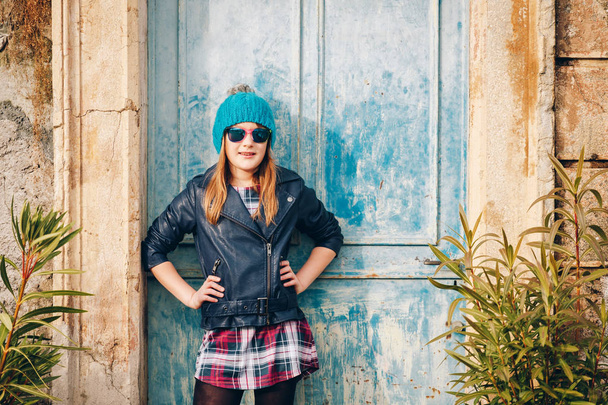 Outdoor-Modeporträt eines lustigen 9-10 jährigen Mädchens mit Sonnenbrille und blauer Lederjacke - Foto, Bild