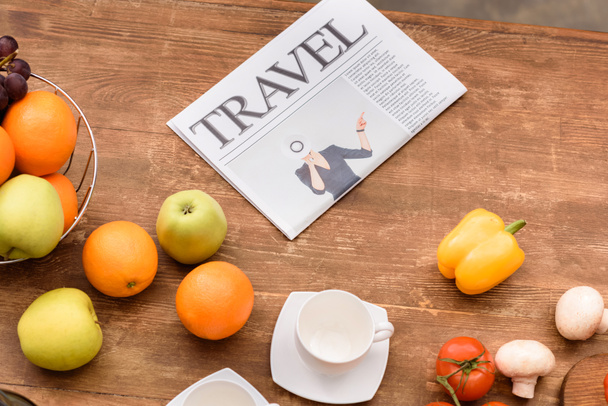 high angle view of travel newspaper and fruits with vegetables on wooden table - Photo, Image