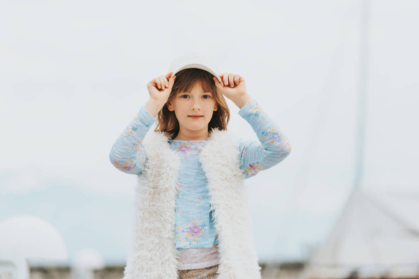 Szabadtéri divat-portré fiatal preteen gyerek lány visel fehér sapka, műszőrme gilet, játszik a port, tónusú képek - Fotó, kép