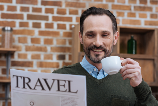 handsome man holding cup of coffee and reading travel newspaper - Fotó, kép