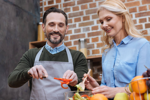 happy affectionate couple preparing salad in kitchen - Photo, Image