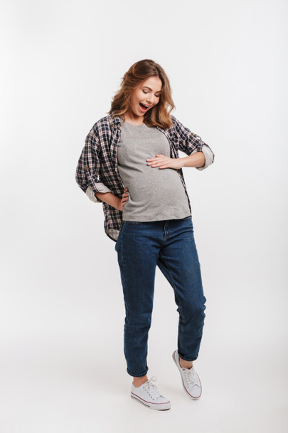 mujer embarazada emocionada mirando barriga aislada en gris
 - Foto, Imagen