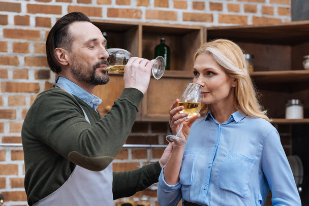 husband and wife drinking wine from glasses in kitchen - Foto, Bild