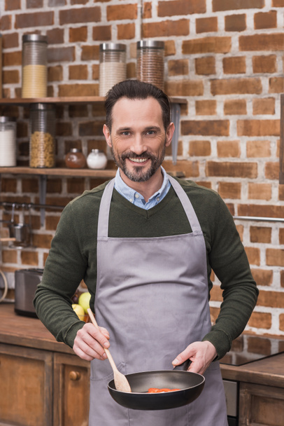 handsome man with frying pan and wooden spatula looking at camera - Foto, Imagem