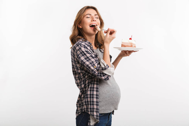 щаслива молода вагітна жінка їсть торт ізольовано на білому
 - Фото, зображення