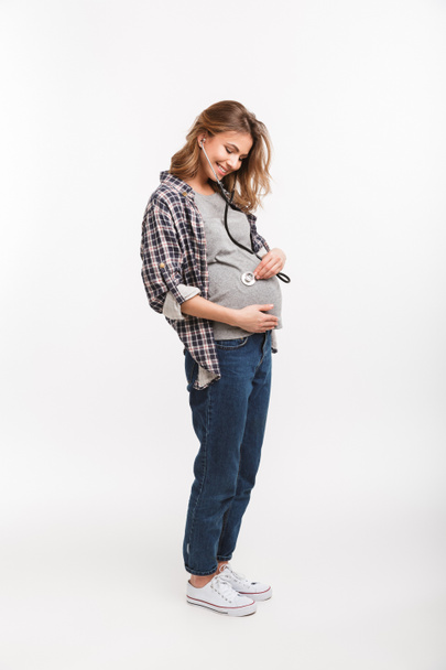 boldog terhes nő hallgató hasa elszigetelt fehér sztetoszkóp  - Fotó, kép