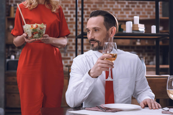 rajattu kuva vaimo tarjoilee pöydän herkullinen salaatti ja aviomies juo viiniä romanttisella illallisella
 - Valokuva, kuva