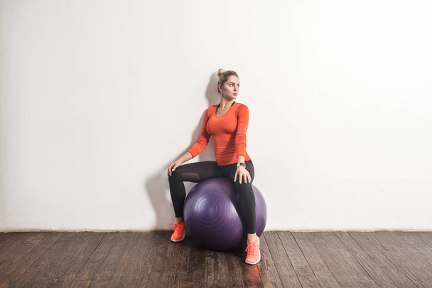 blonde woman sitting on fitness bal near light gray wall - Valokuva, kuva