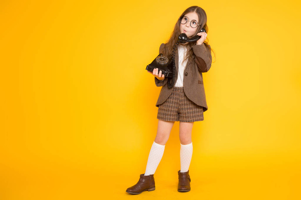 Cute little brunetka dziewczyna rozmawia stary telefon na żółtym tle  - Zdjęcie, obraz