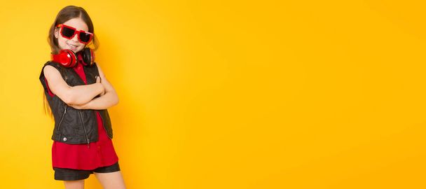 Cute little brunette girl with modern red headphones on yellow studio background  - Foto, imagen