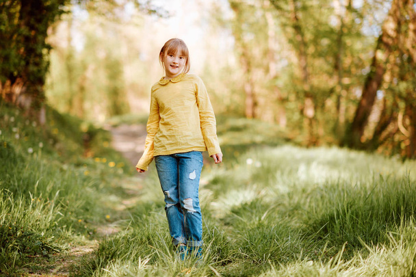 Outdoor portrait of pretty little girl in spring forest, wearing green blouse and jeans - Photo, Image