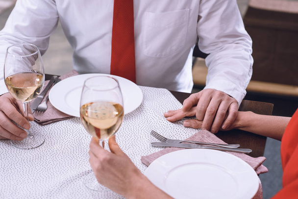 cropped image of couple holding hands and glasses of wine at romantic date - Фото, зображення