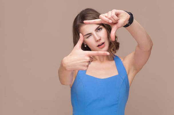 woman in blue dress showing perspective frame on light brown background - Foto, afbeelding